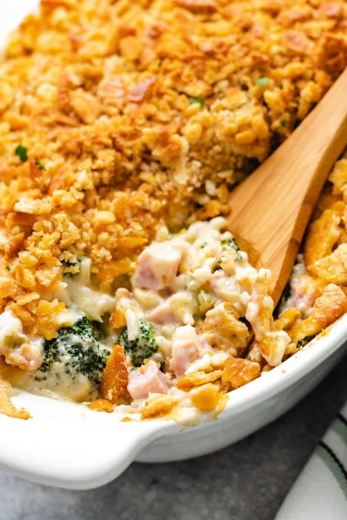 Wooden spoon scooping casserole out of a dish.