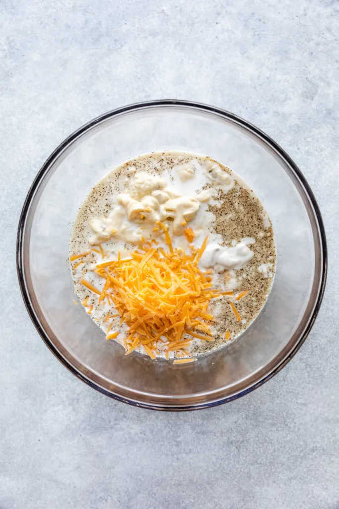 Milk, cheese seasonings, and canned soup in a bowl.