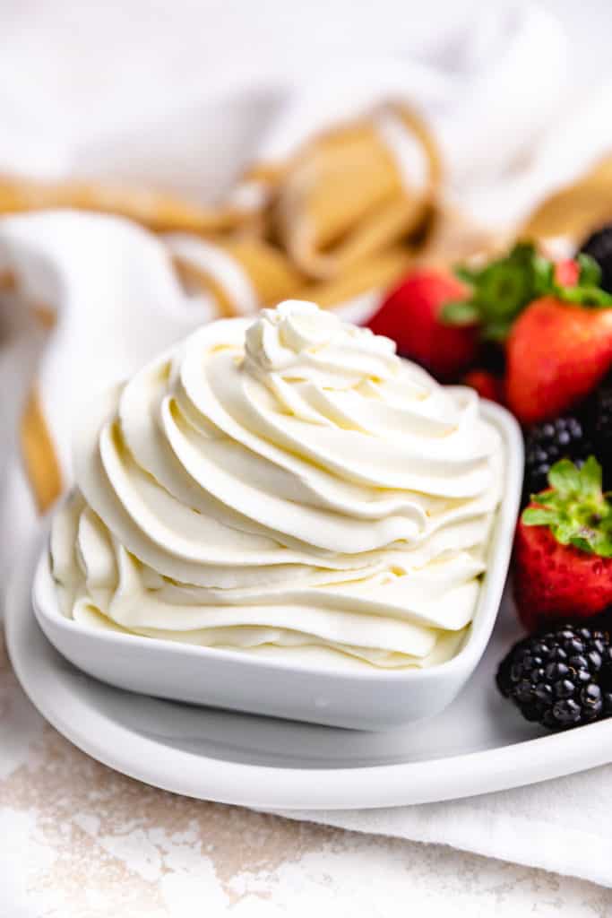 Fruit next to a bowl of whipped cream.