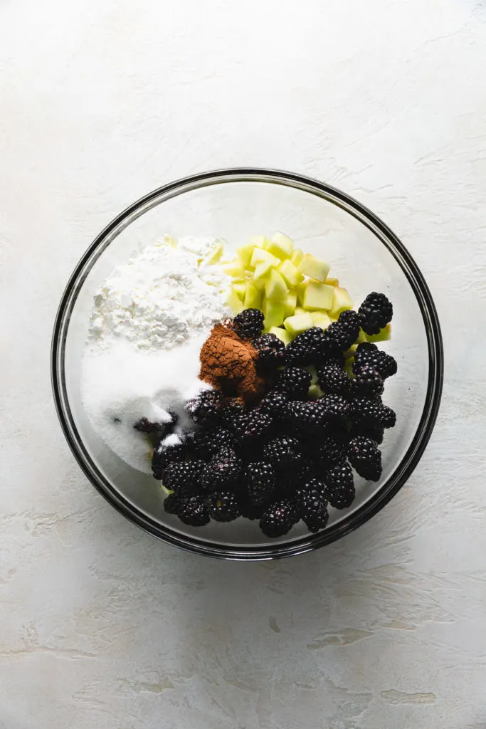 Flour, sugar, spices, apples, and blackberries in a bowl.