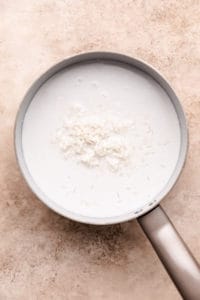 Rice poured into a pan of coconut milk, coconut water, and sugar.