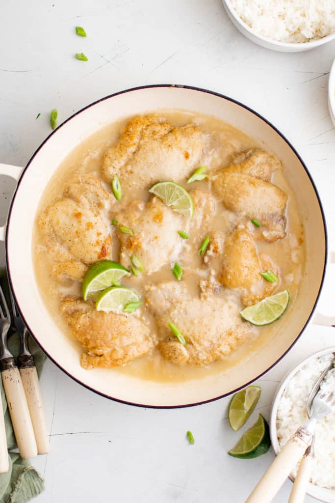 Pan of coconut chicken with lime wedges.
