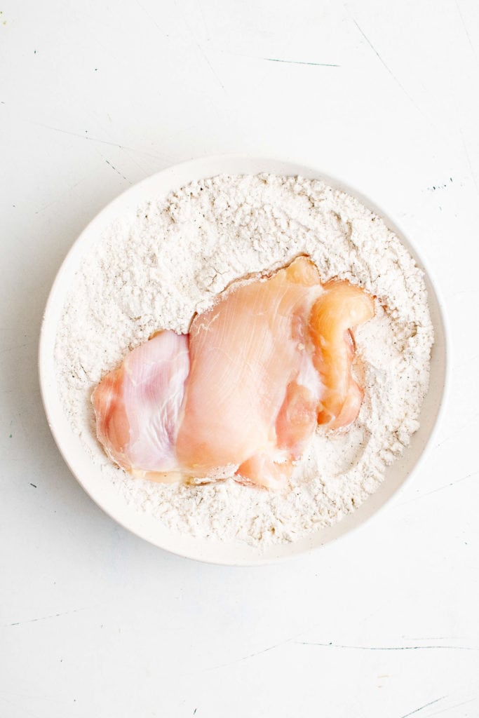 Chicken thigh in a dish of seasoned flour.