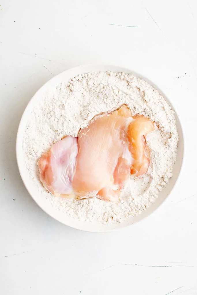 Chicken thigh in a dish of seasoned flour.