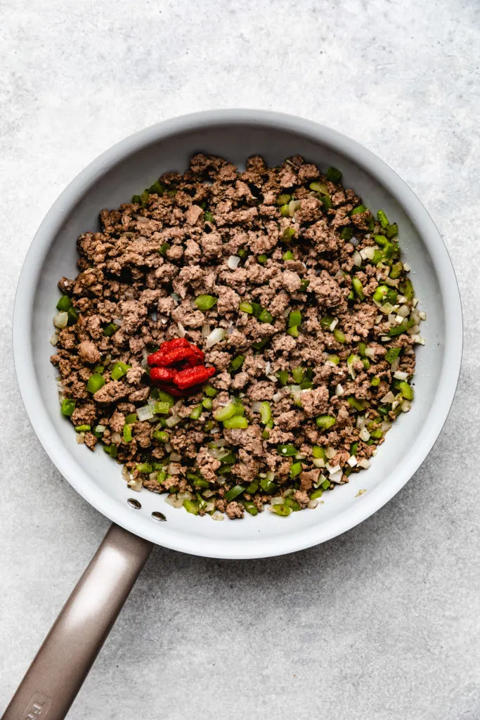 Ground beef, peppers, onion, and tomato paste in a skillet.