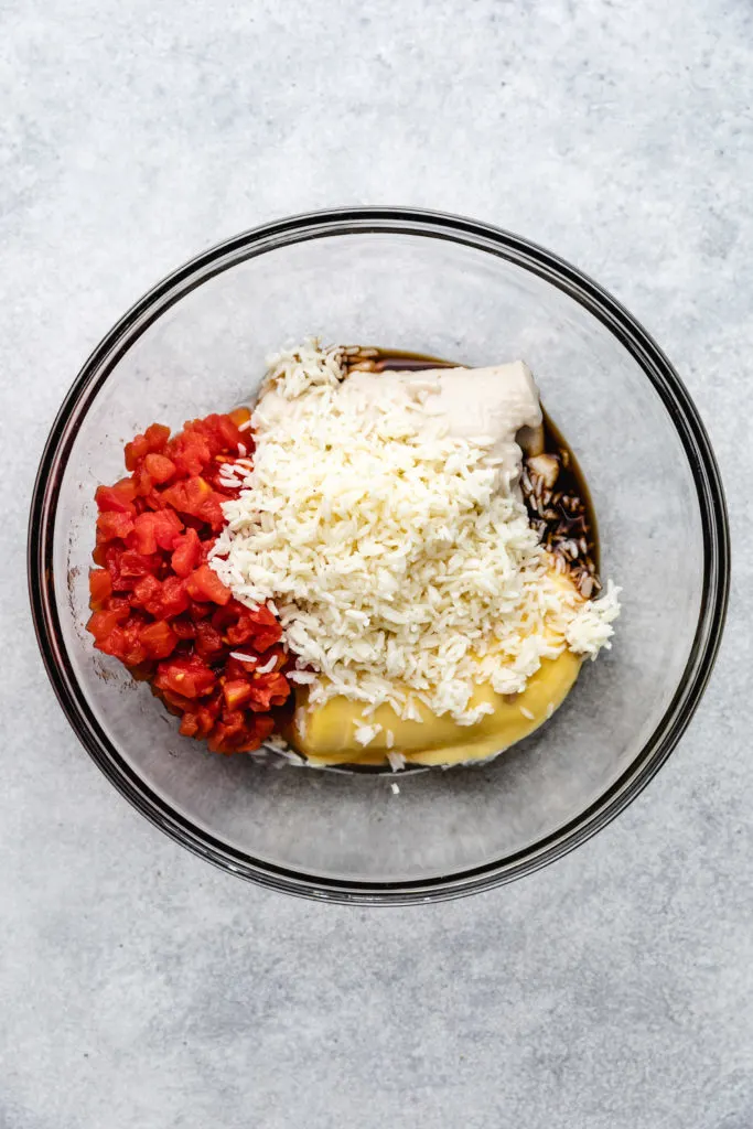 Cream of soups, rice, diced tomatoes, and seasonings in a bowl.