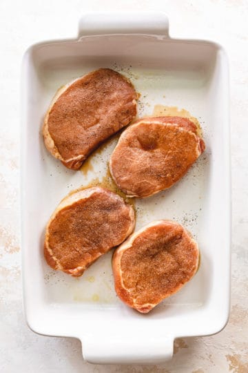 Marinated pork chops with salt and pepper in a baking dish.