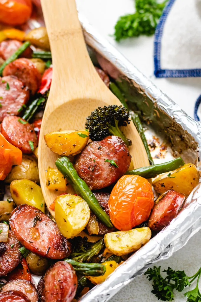 Wooden spoon scooping veggies and sausage off a pan.