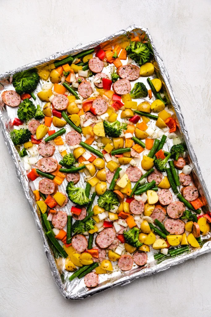 Sheet pan filled with unbaked seasoned sausage rounds and cut vegetables.