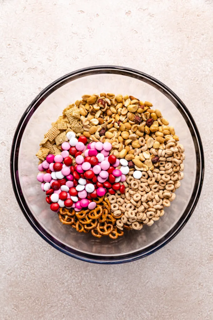 Glass bowl filled with cereal, peanuts, m&ms, and pretzels.