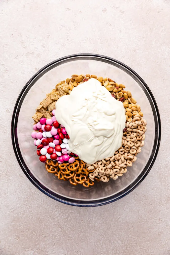 Melted vanilla candy poured over a bowl of snack mix ingredients.