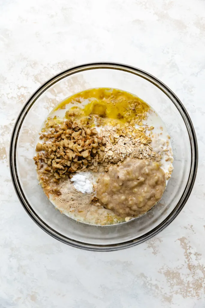 Top down view of oats, bananas, nuts, butter, and milk in a bowl.