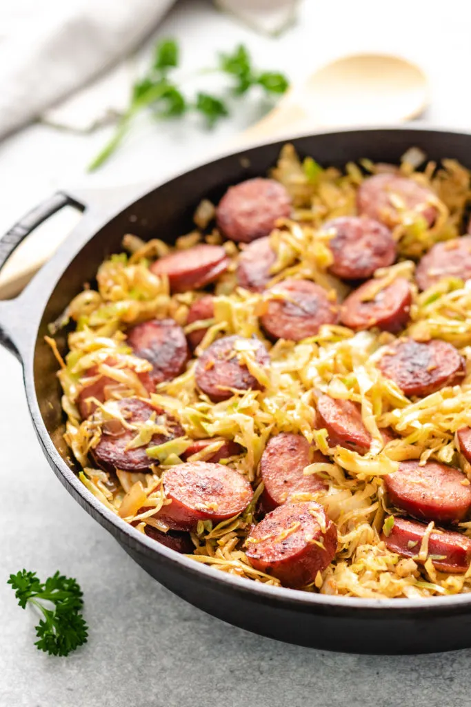 Side view of kielbasa and fried cabbage in a pan.