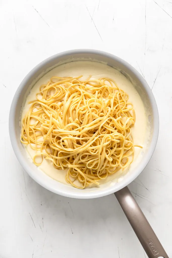 Noodles added to a pan of garlic parmesan sauce.