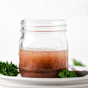 Side view of a jar of salad dressing with poppy seeds.
