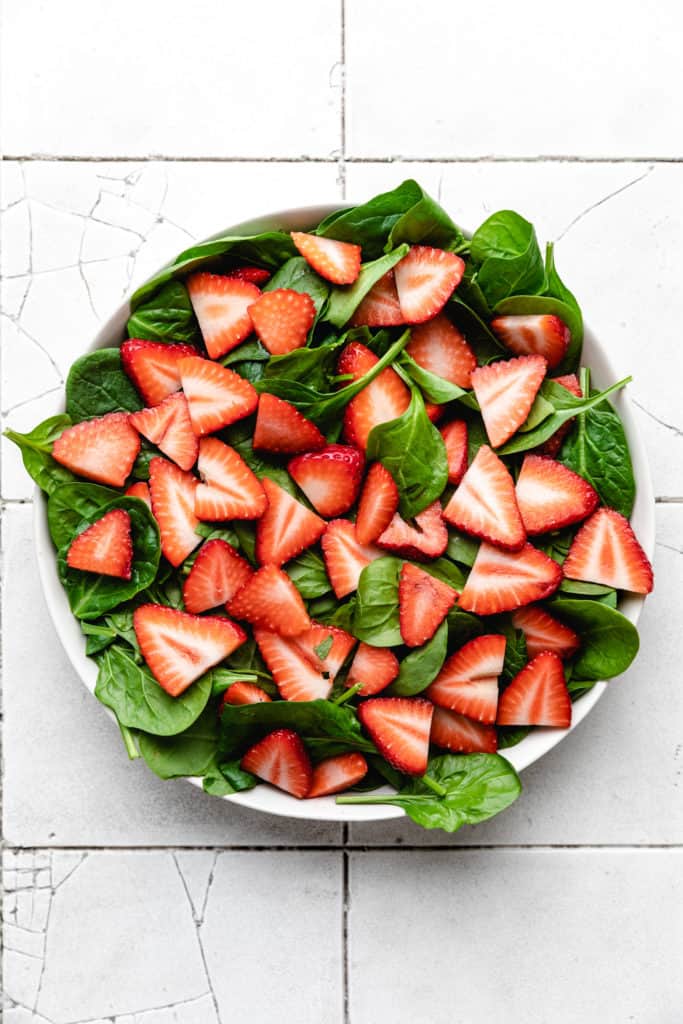 Strawberry slices on top of a bowl of spinach.