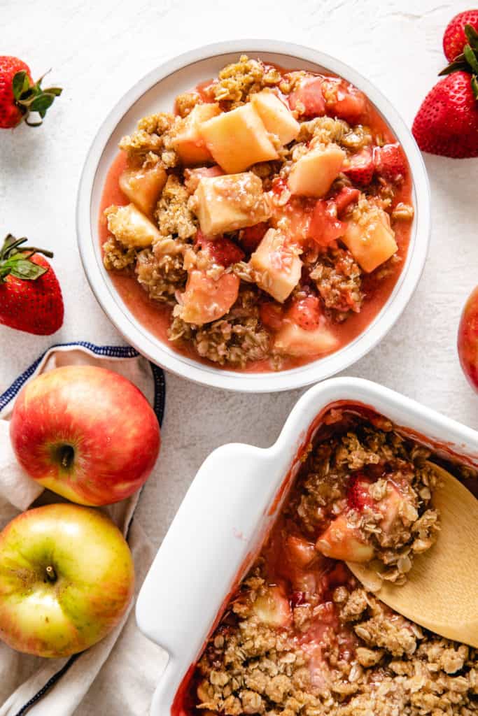 Top down view of apple crisp with strawberries next to fresh fruit.