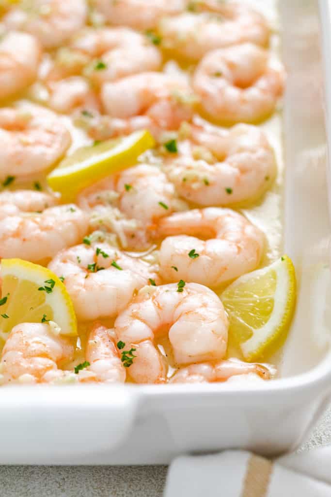 Side view of lemon wedges in a pan of baked shrimp.