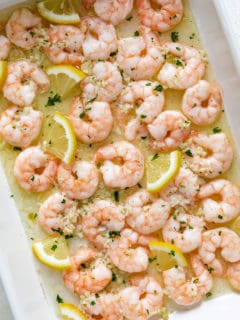 Close up view of baked shrimp with lemon butter and lemon slices in a pan.