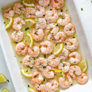 Close up view of baked shrimp with lemon butter and lemon slices in a pan.