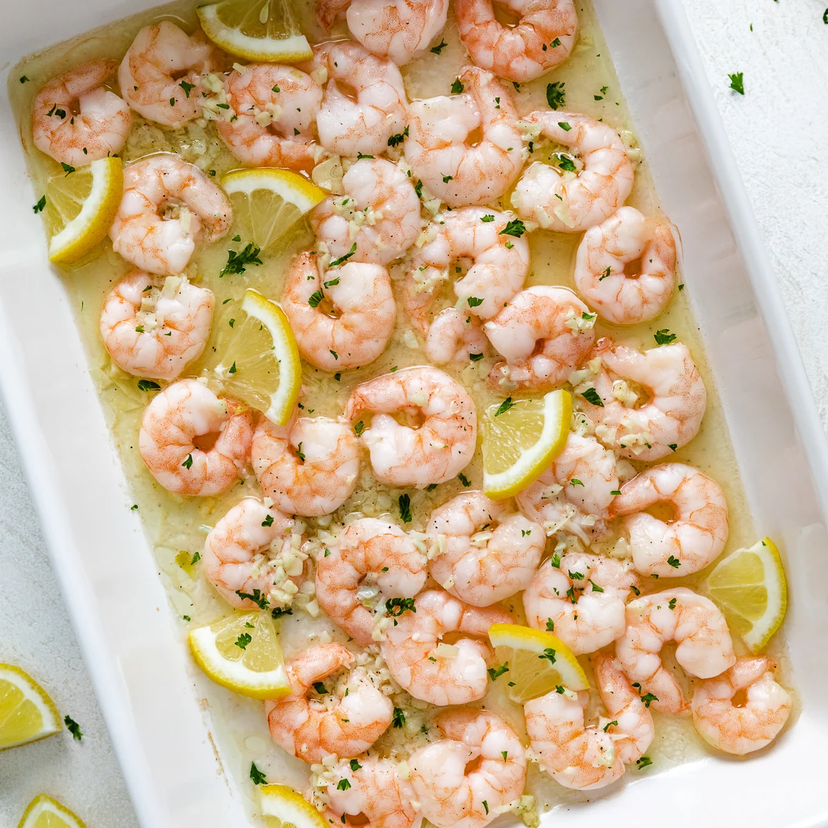 Close up view of baked shrimp with lemon butter and lemon slices in a pan.