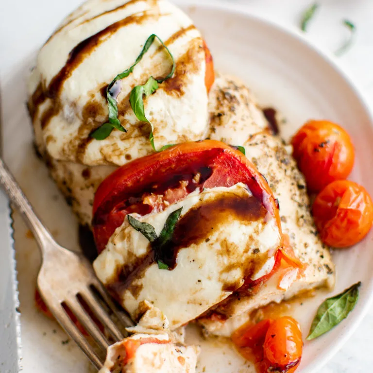 Close up view of a chicken breast with mozzarella, tomatoes, and basil.