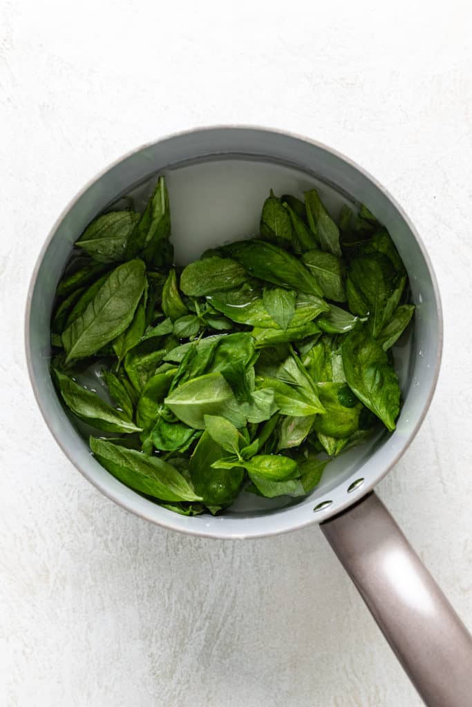 Top down view of basil, sugar and water in a pan.