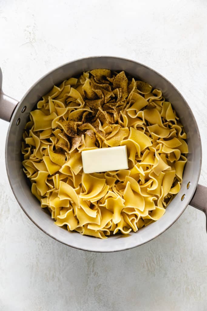 Salt, pepper, and butter on top of a pan of egg noodles.