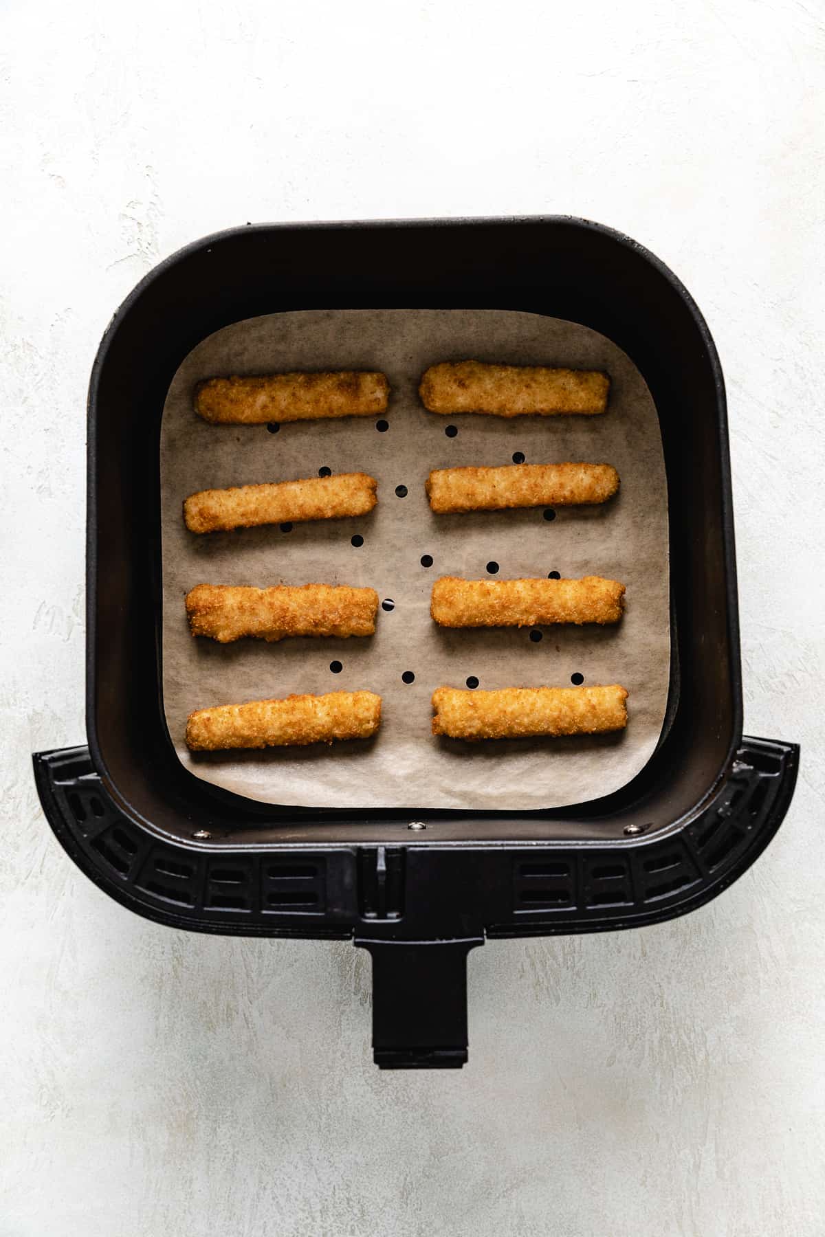 Eight frozen fish sticks in an air fryer.