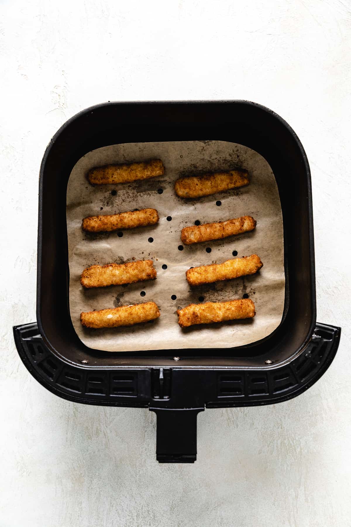Air fryer basket holding 8 fish sticks.