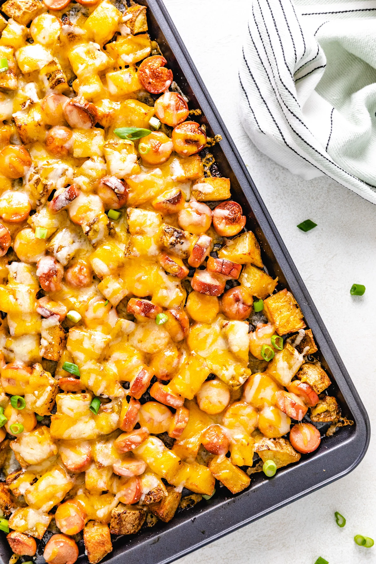 Top down view of potatoes, hot dogs and cheese on a pan.