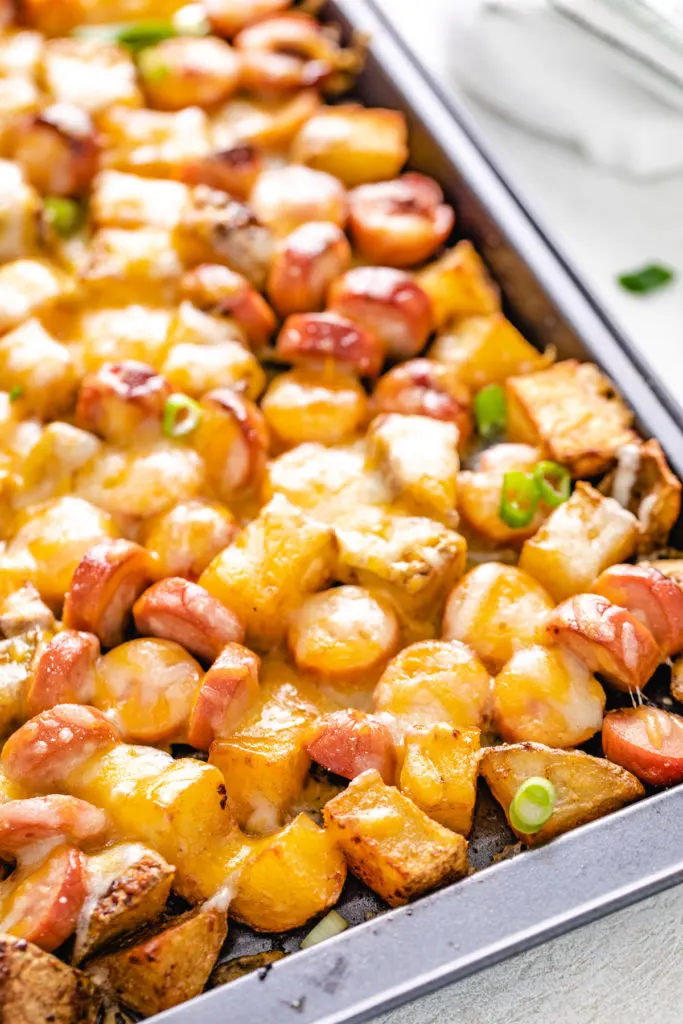 Angled view of cheesy hot dogs and potatoes on a sheet pan.