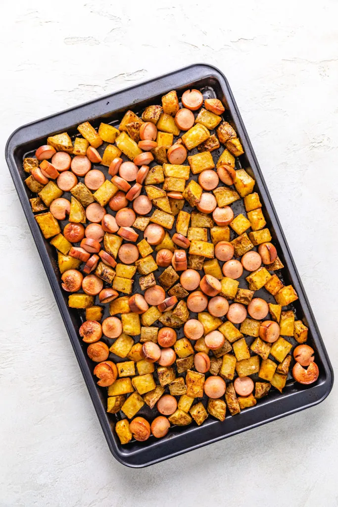Roasted potatoes and caramelized hot dogs on a baking sheet.