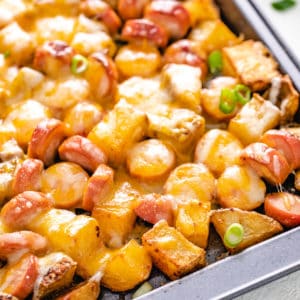 Close up view of cheesy potatoes and hot dogs and a sheet pan.