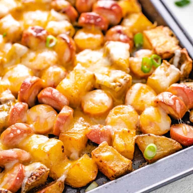 Close up view of cheesy potatoes and hot dogs and a sheet pan.