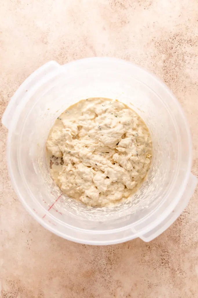 Bread dough with fresh thyme in a plastic food bucket.