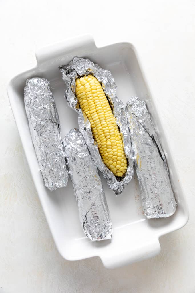 Four ears of corn in foil with one open.