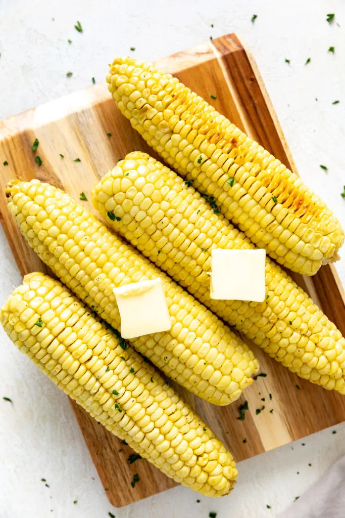 Top down view of 4 ears of corn on a cutting board.