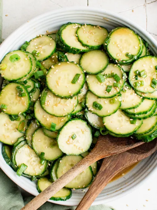 Top down view of a plate of cucumber salad with two wooden spoons.