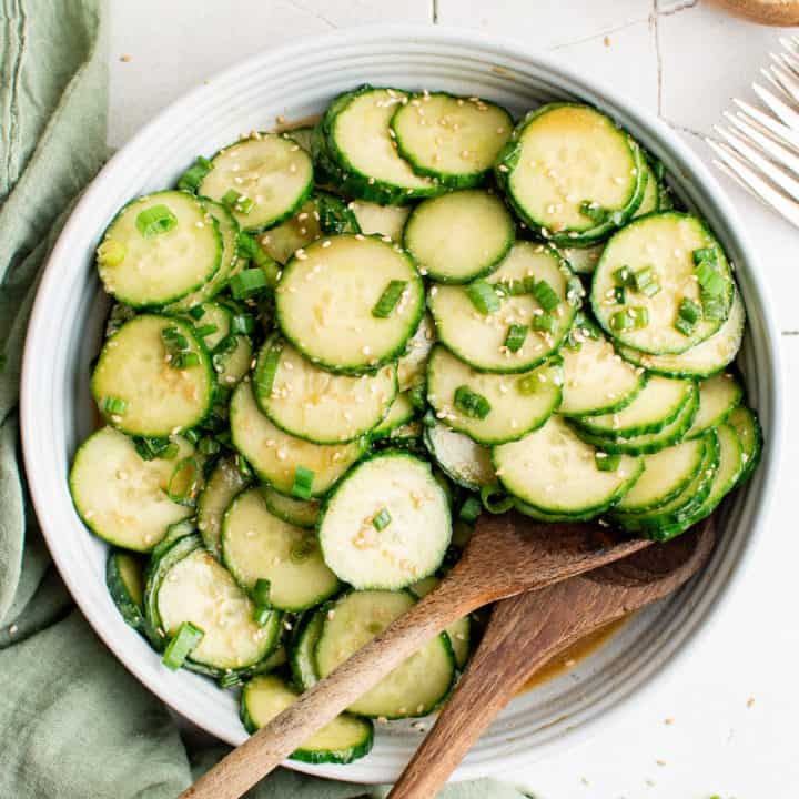 Top down view of a plate of cucumber salad with two wooden spoons.
