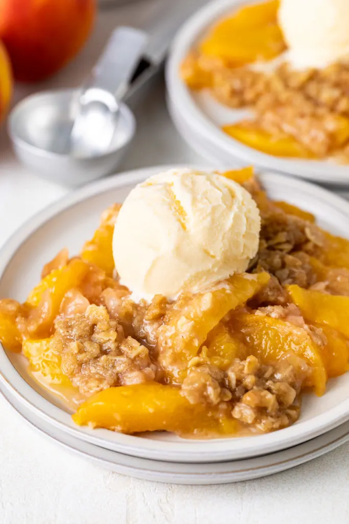 Peach crisp with vanilla ice cream on plates.