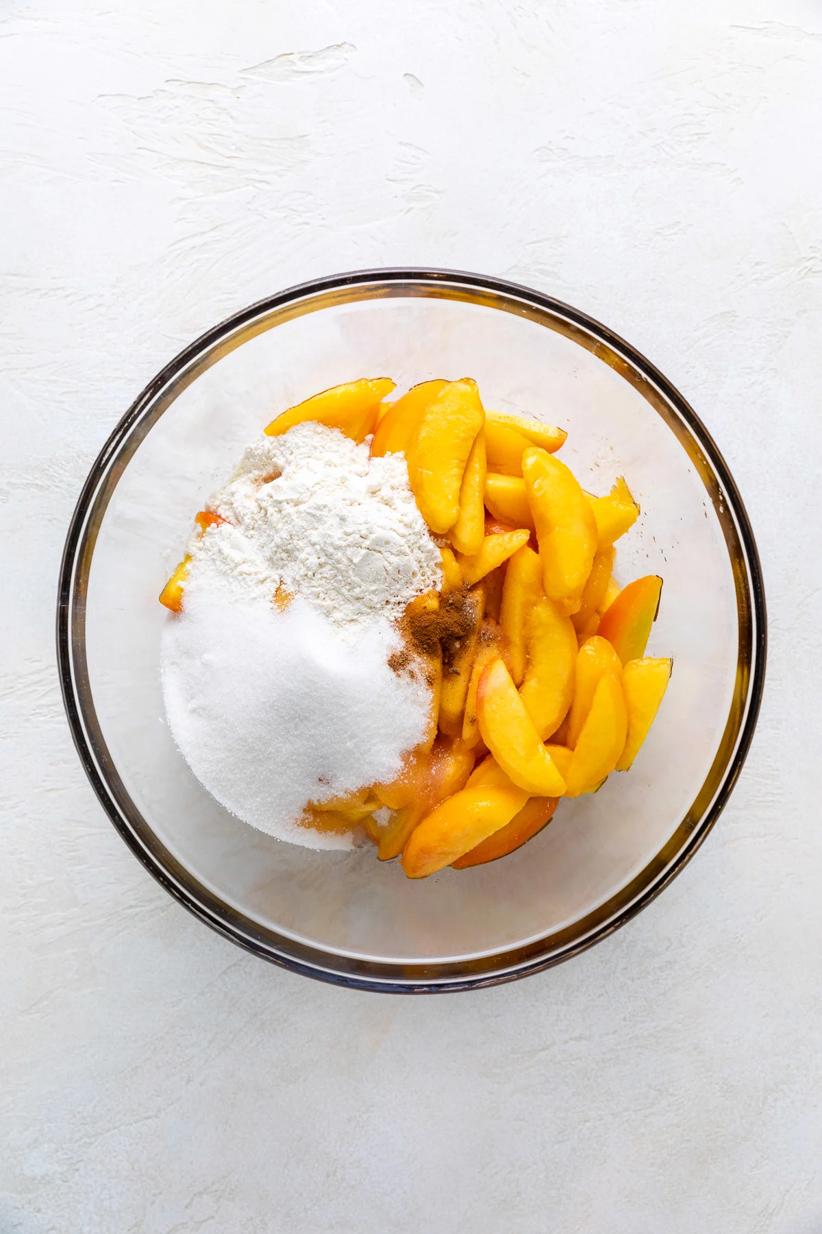 Sugar, flour, peaches, and seasoning in a glass bowl.