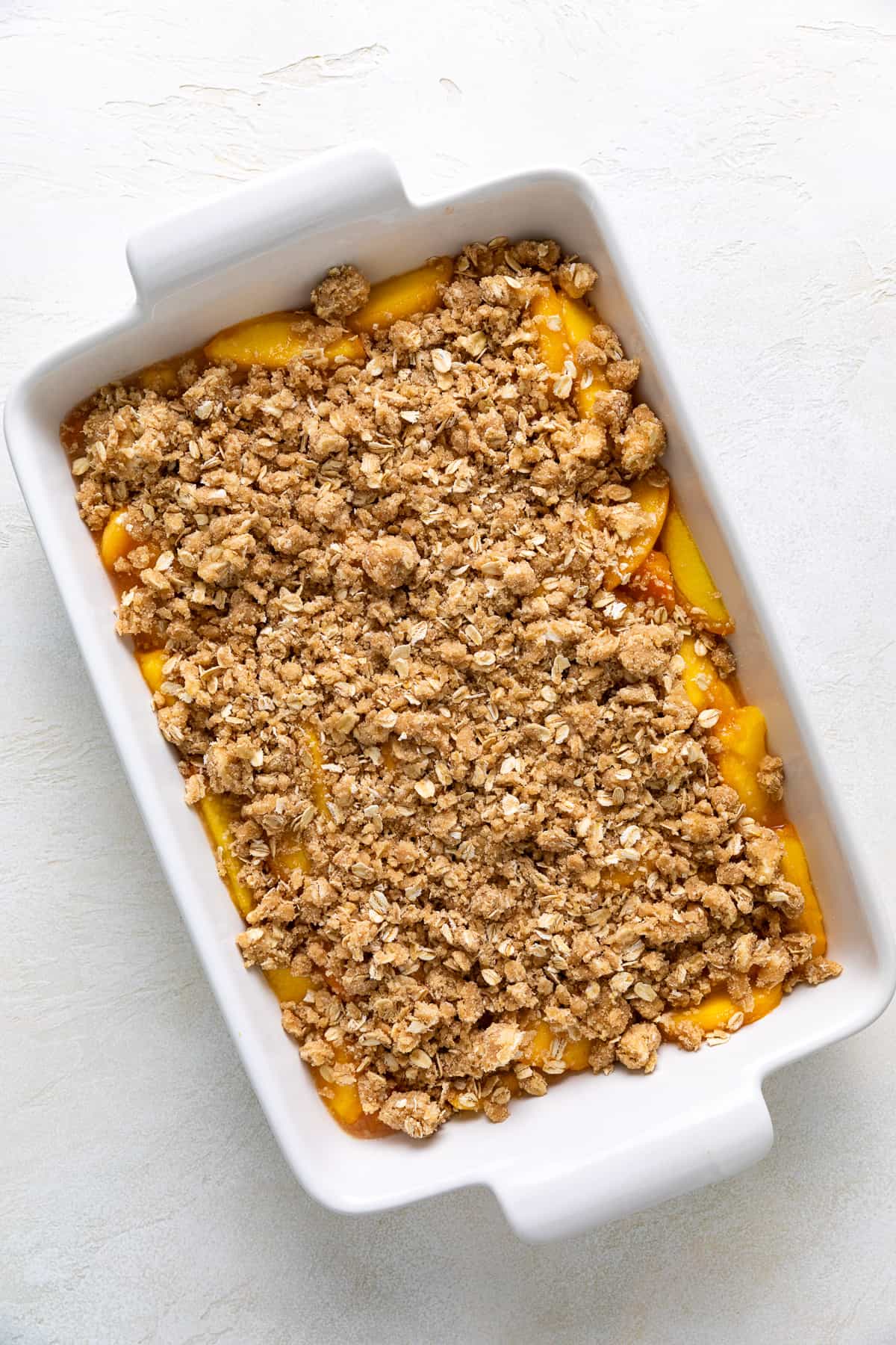 Crumble topping on top of peach filling in a pan.