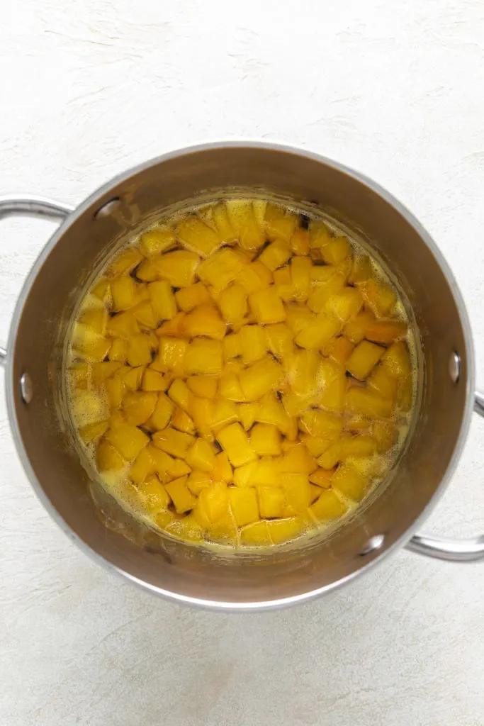 Peaches, water, and sugar cooking in a pan.