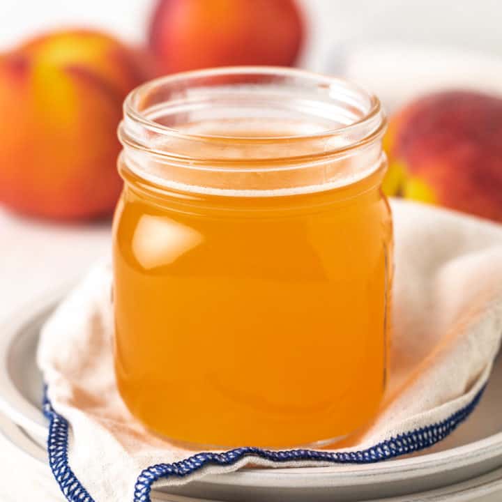 Side view of two plates holding a jar of peach simple syrup.