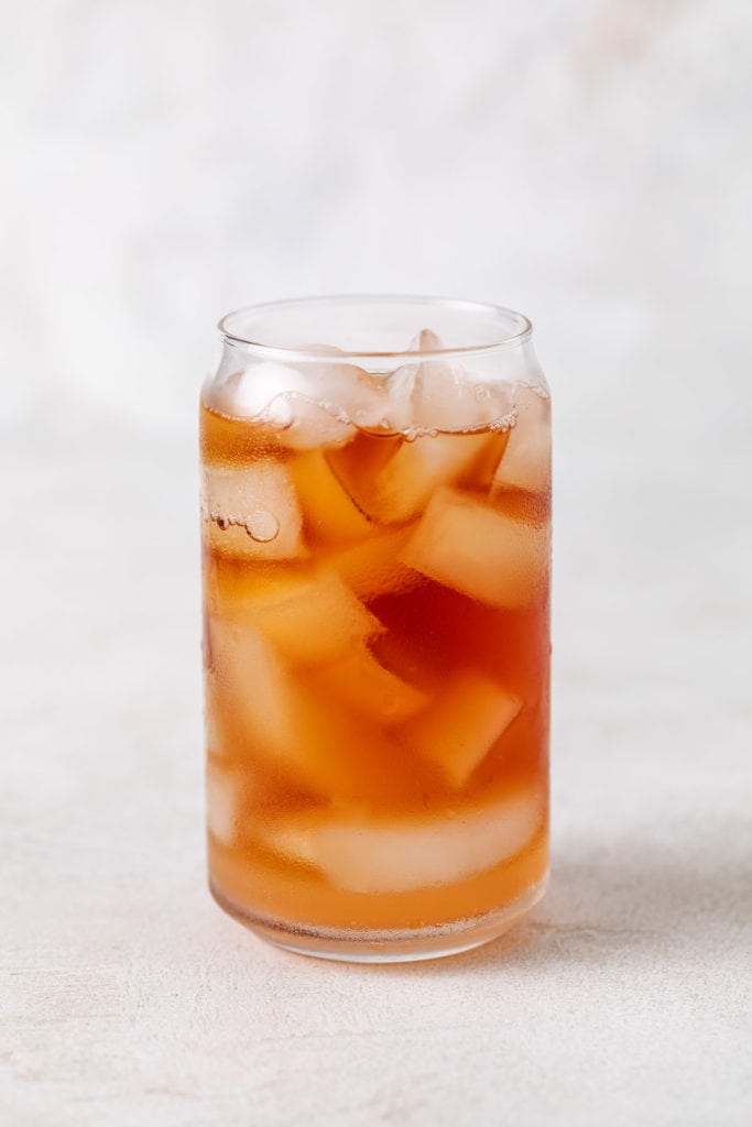 Freshly brewed iced tea poured into a glass with peach syrup.