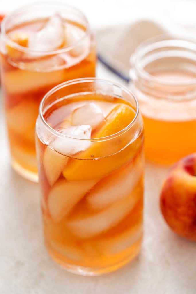 Tall glass of freshly brewed peach tea with ice and frozen peaches.