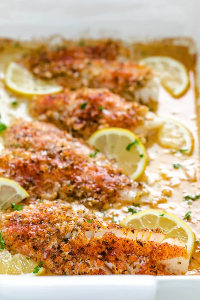 Side view of a pan of seasoned fish with sliced lemons.