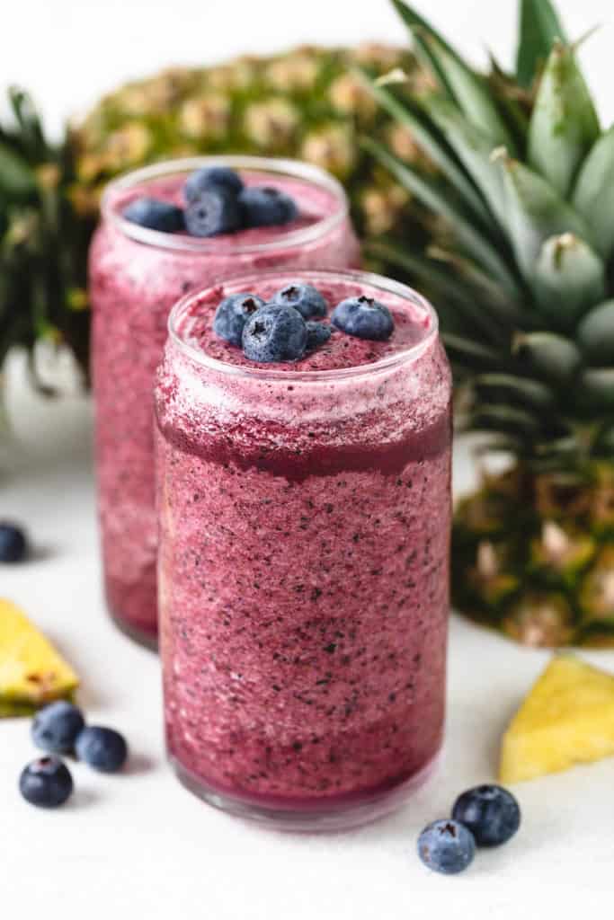 Two glasses of blueberry smoothie with pineapple.