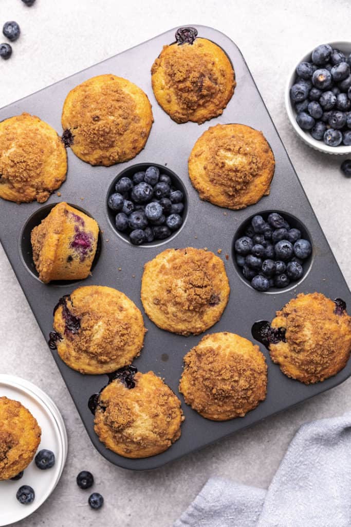 Close up view of muffins and blueberries in a muffin pan.